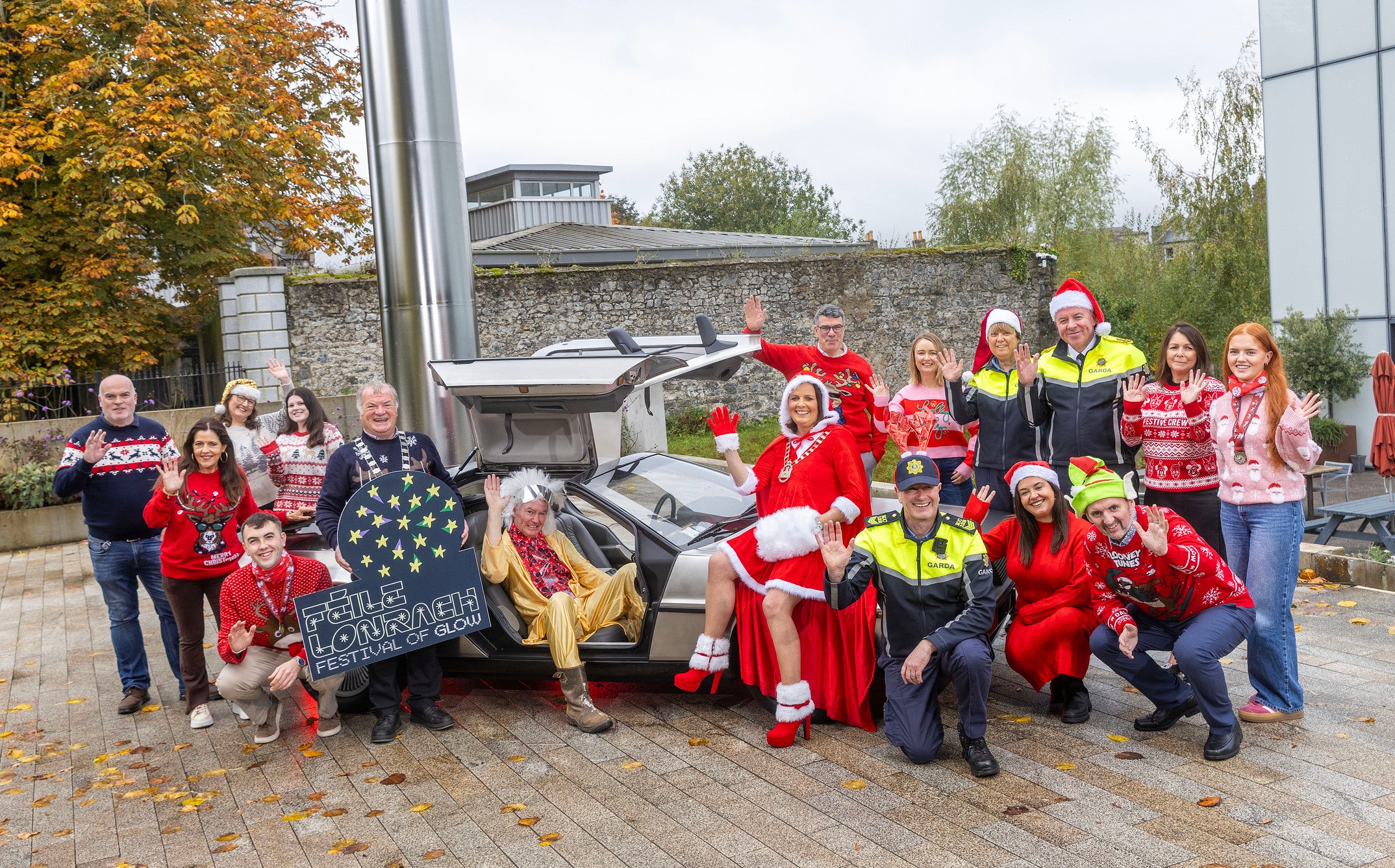 Féile Lonrach – Festival of Glow, Carlow - a group of smiling and waving people in Christmas jumpers around a silver sports car.