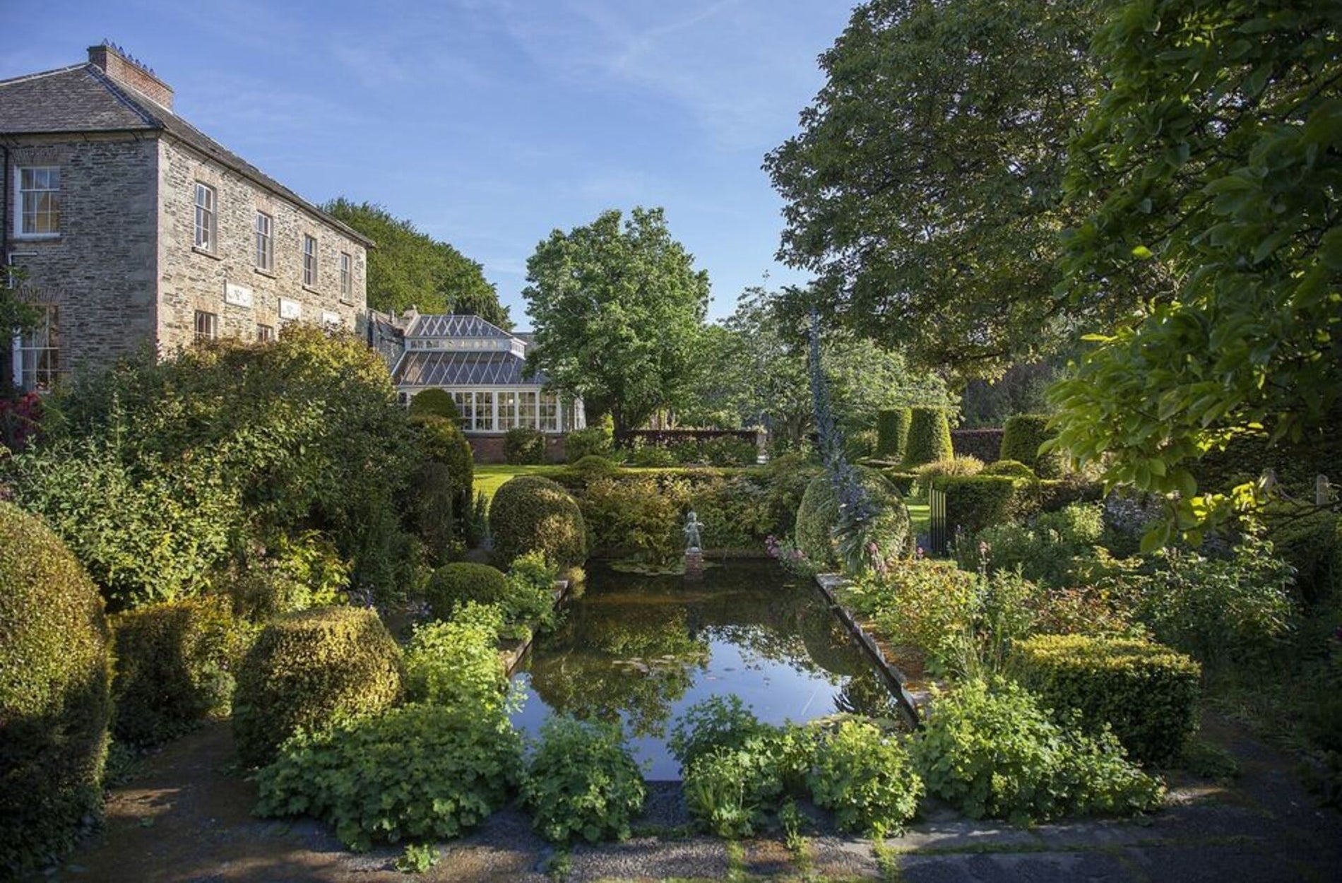 A large country house with a garden pond framed with shrubs and plants