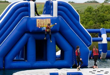 Large blue outdoor inflatable water obstacle course with people in red life jackets