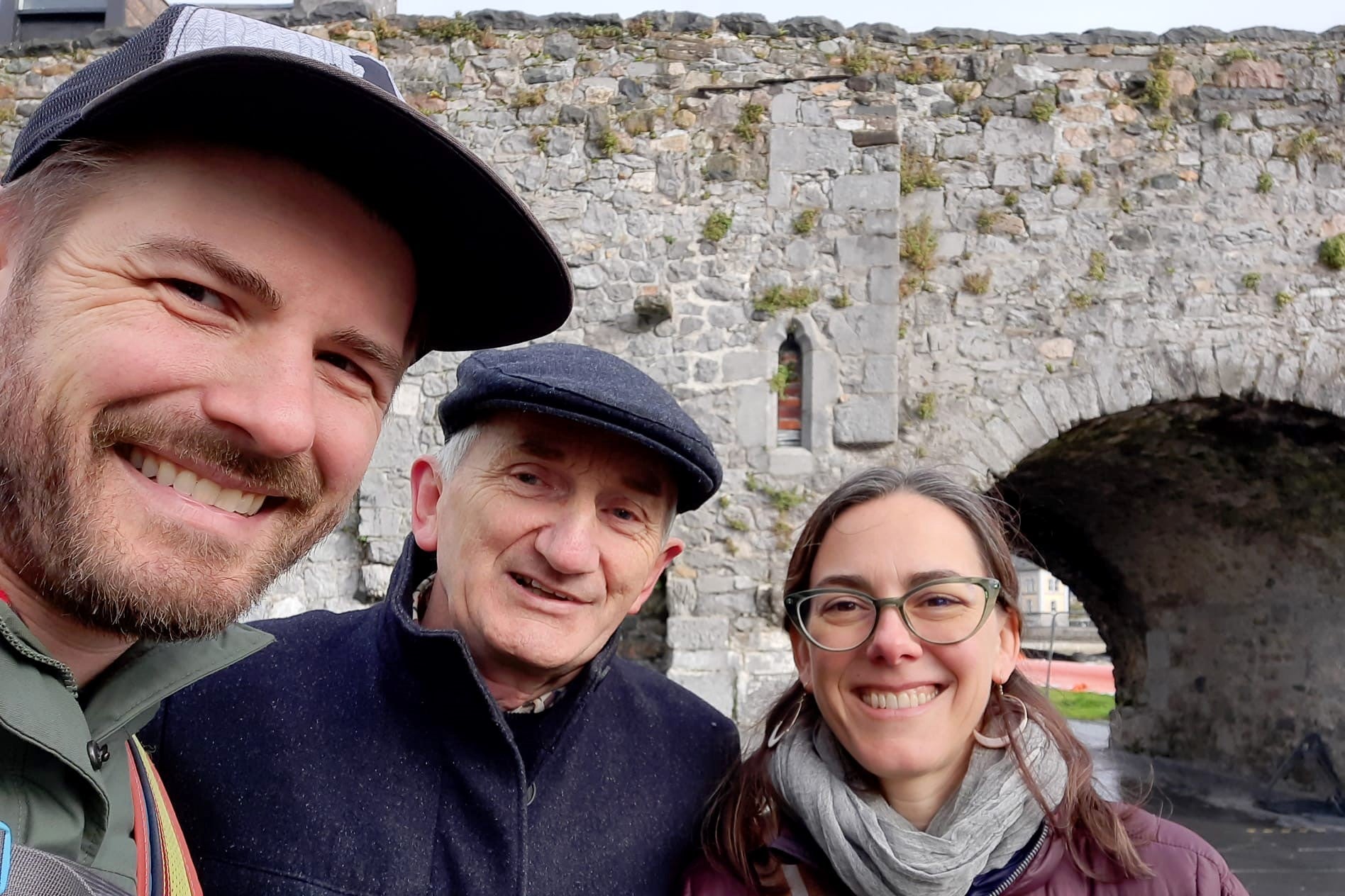 Three people smiling standing to the side of a stone archway