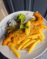 A plate of fish and chips served with tartar sauce and mushed peas