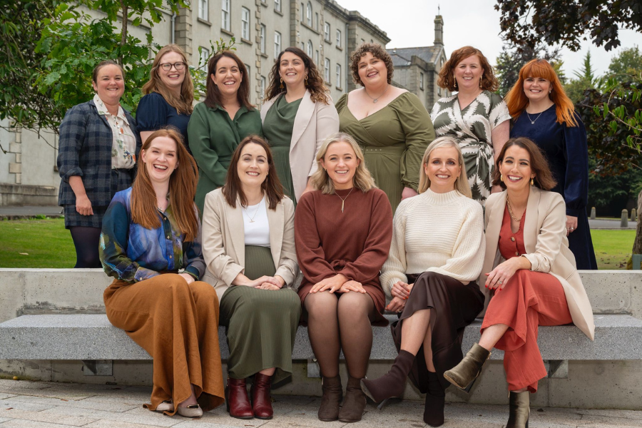 enCÓRe at Christmas, a group of smiling women seated on and standing behind a concrete bench outside a building
