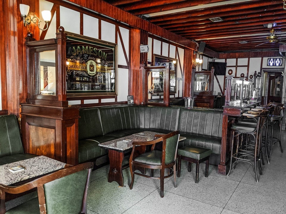 Pub with green leather chairs and seats and wooden tables and the bar with bar stools towards the back