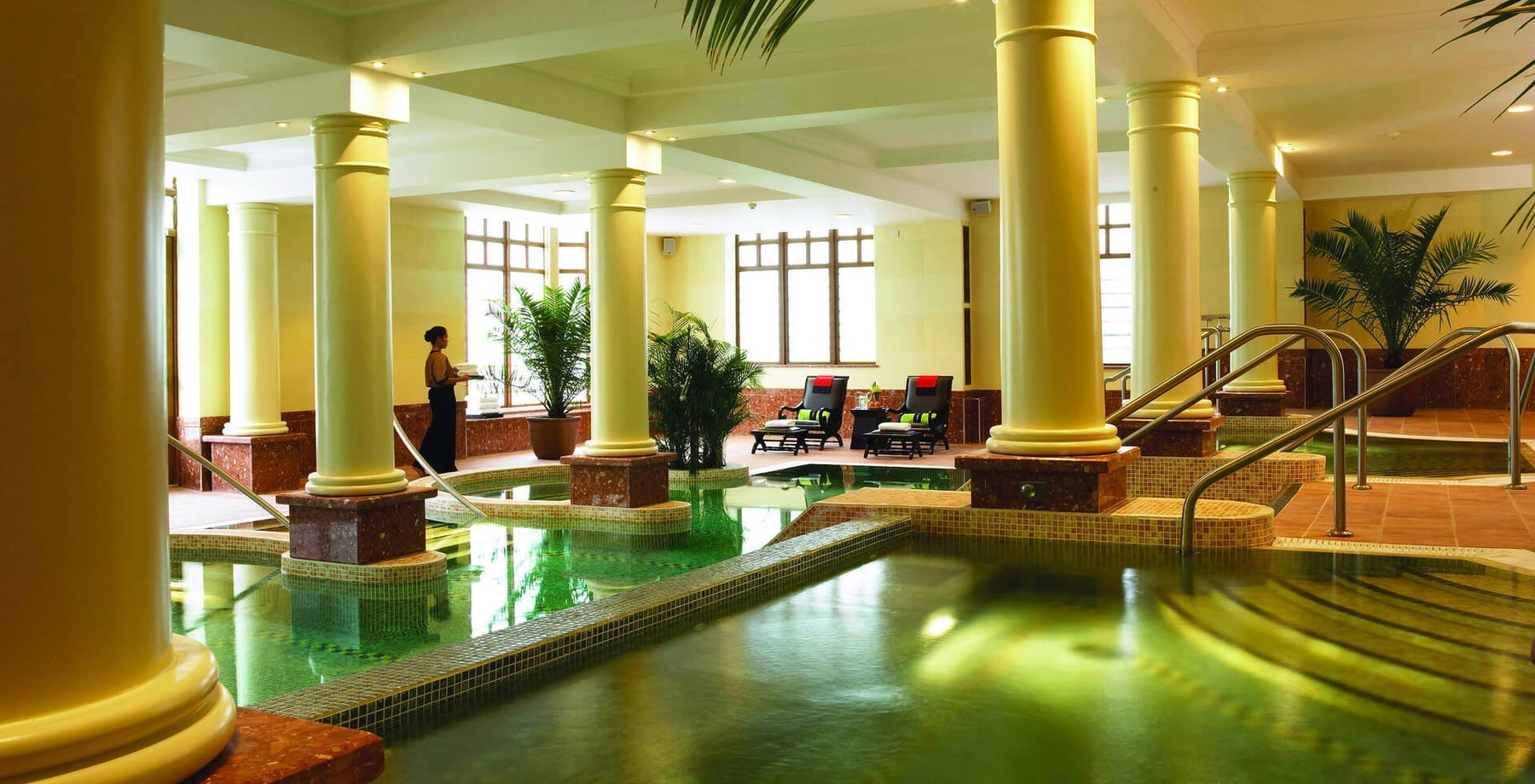 A large room in a spa with tall pillars and a pool