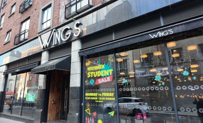 Exterior of a restaurant with lots of windows and black awning over a wooden door