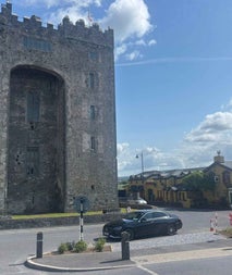 Luxury car parked outside a large castle with a yellow bar and restaurant to the right