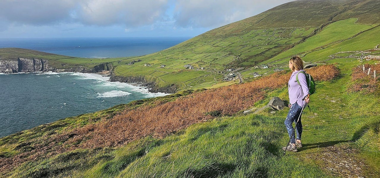 Person holding a walking pole standing in a field overlooking the sea