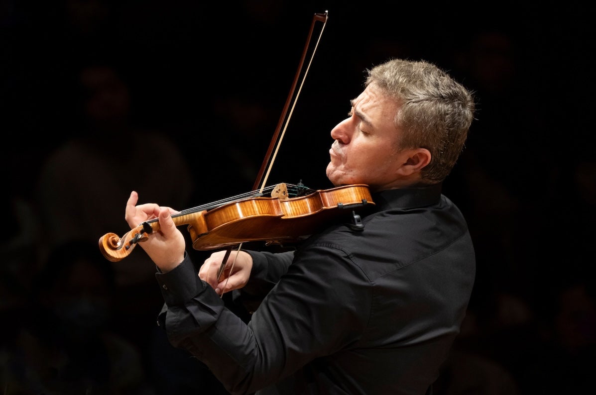 Side view of a man playing a violin with emotion, against black plain background.