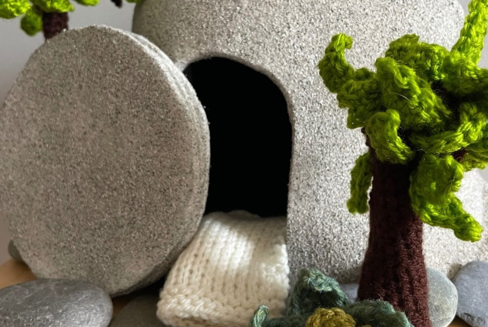A stone tomb, open, with knitted trees and smaller stones surrounding it.