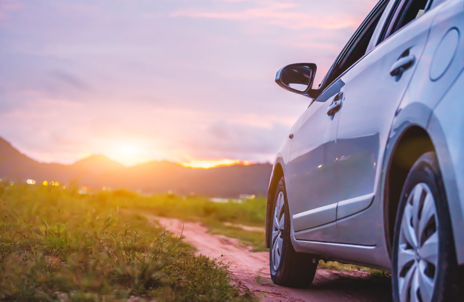Small silver car on a country dirt track facing sunset