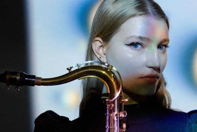 A head and shoulders view of a serious woman holding a saxophone upright in front of her.