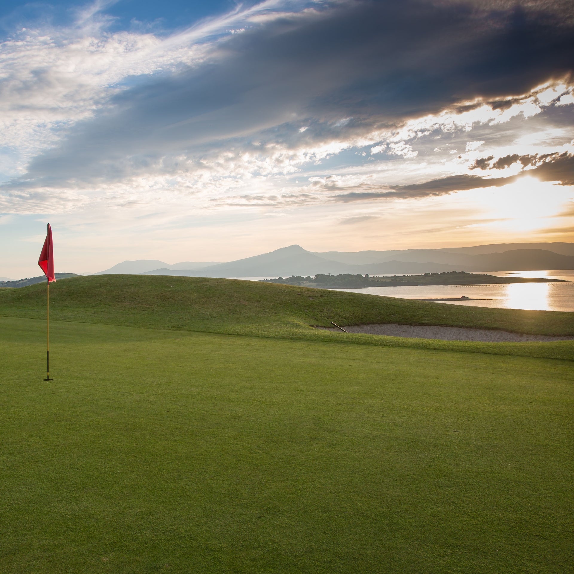 Red flag on a golf course overlooking the water at sunset