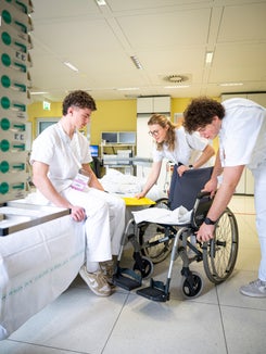 Sieht einfacher aus, als es ist: Manuel und Isabel helfen Lukas vom Krankenhausbett in den Rollstuhl und erproben dabei selbst die Rolle von Patient und Pflegekraft. (Foto: Fabio Brucculeri)