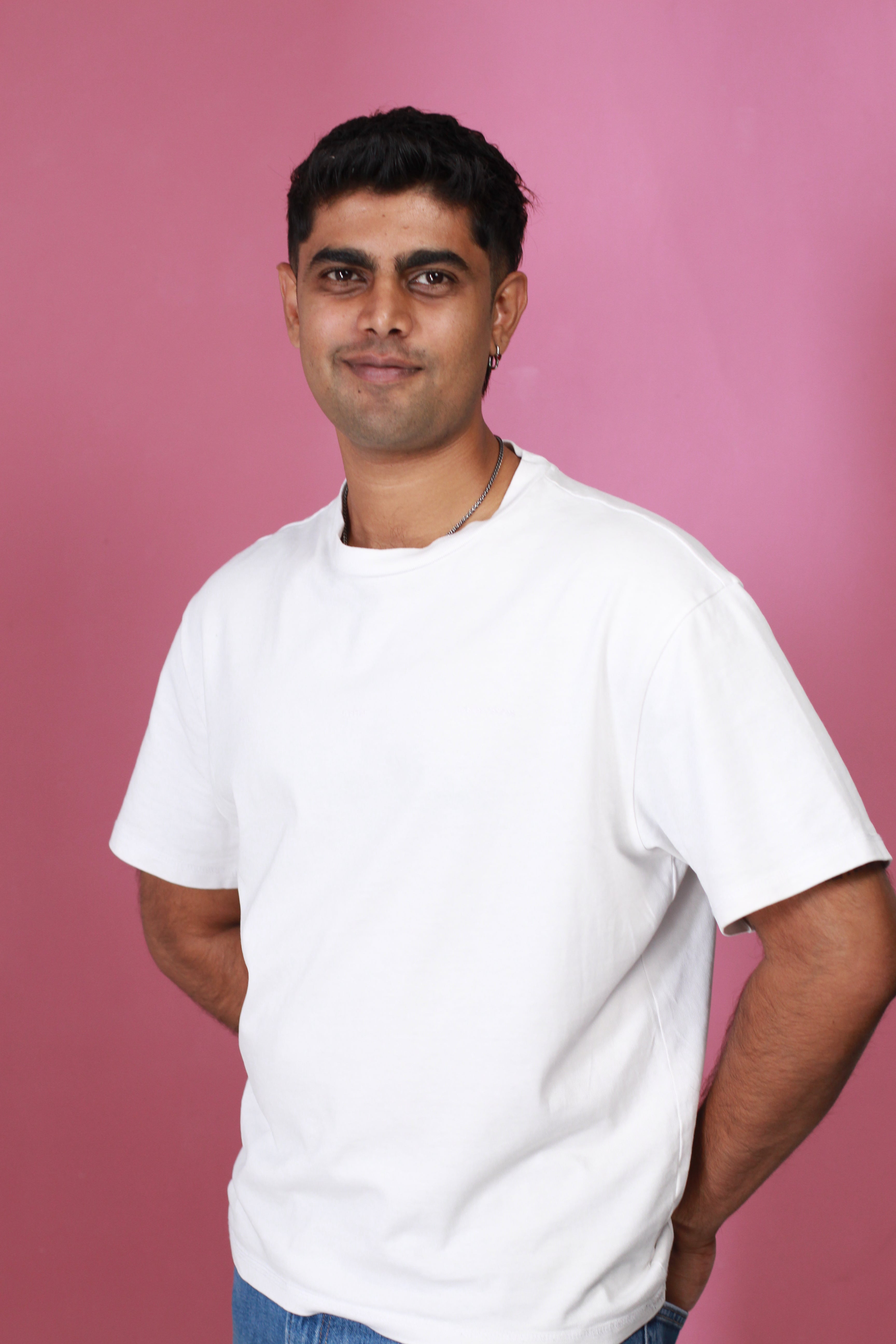 Award-winning South African comedian and author Prev Reddy smiling in a white t-shirt against a vibrant pink background, official author photo for his debut memoir, Qualified Disappointment.