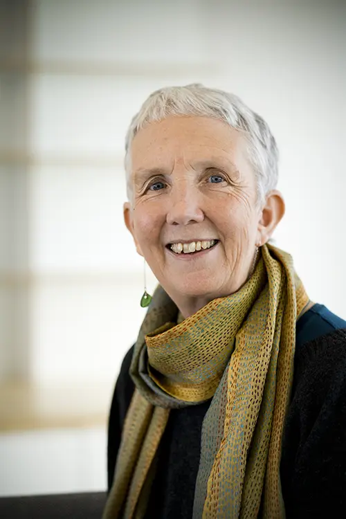 Photograph of Ann Cleeves smiling in a green and yellow scarf and dark grey jumper
