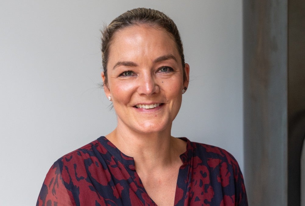 Katharina Harf, Chair of the Foundation Board and Global CSO of DKMS, smiles at the camera with her hair pulled back, wearing a red and dark blue patterned blouse.