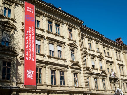 Un banner ben visibile sulla facciata di Palazzo Widmann a Bolzano annuncia il significativo anniversario 2026, che celebra gli 80 anni del Trattato di Parigi. (Foto: USP/Fabio Brucculeri)