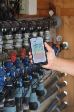 Eine sensorbasierte Bewässerung misst permanent die Feuchtigkeit oder Saugspannung im Boden und steuert die Wasserzufuhr vollautomatisch nach Bedarf. Anstatt nach fetsgelegtem Zeitplan zu gießen, erhalten Pflanzen exakt dann Wasser, wenn ein kritischer Trockenheitswert unterschritten wird. Im Bild die Statistik auf dem Mobiltelefon, links die Steuerventile. (Foto: LPA/Maja Clara)