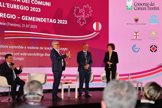 Die Übergabe der Glocke und damit des Vorsitzes des Euregio-Rates der Gemeinden von Paride Gianmoena (Trentino) an Südtirols Gemeindenpräsident Andreas Schatzer. (Foto: Presseamt Trentino/Juliet Astafan)