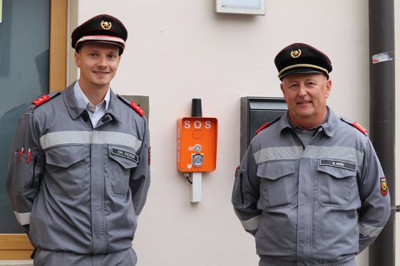 All’esterno della sede dei vigili del fuoco volontari di Cardano è già stato installato il pulsante di emergenza; a sinistra nella foto, il comandante Christoph Vieider e il presidente dell’Unione dei Copri volontari dei vigili del fuoco Martin Künig. (Foto: USP/Maja Clara)