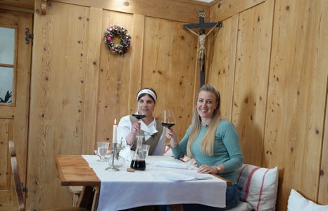 Köchin Giulia Segna (links) und So-isst-Euregio-Moderatorin Karin Gschnitzer stoßen mit dem heimischen Groppello – im Dialekt Gropèl – an. Sprachlich und kulinarisch passt er perfekt zum Tortèl, dem knusprigen Kartoffeltaler. (Foto: Euregio)