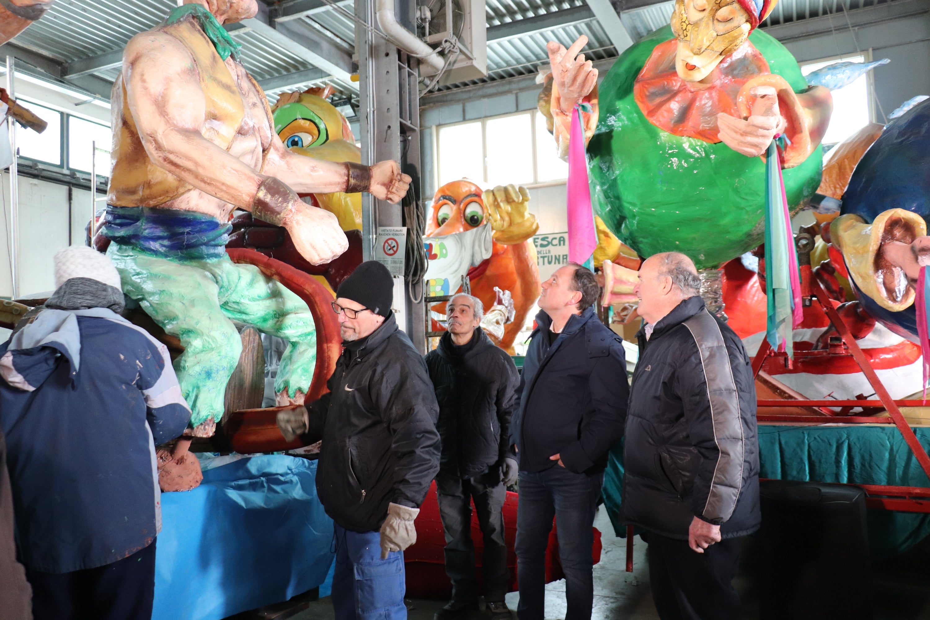 L'assessore Vettorato (nella foto il secondo da destra) insieme al presidente del Gruppo carnevalesco di Laives Cesare Zenorini (primo da destra) visita il tendone a Pineta dove i volontari preparano e custodiscono i carri allegorici. (Foto: ASP)