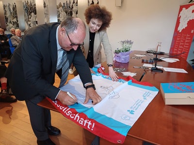 „Jedes Objekt erzählt. Jedes Schweigen sagt uns etwas“, schreibt MITAG-Präsident Oswald Mederle, assistiert von Elisa Bertò, Mitglied des Euregio-Generalsekretariats, auf die Euregio-Museumsjahr-Wanderfahne. (Foto: MITAG)
