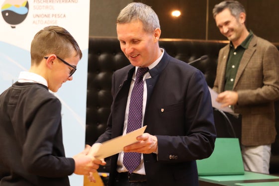 “Pescare significa anche prendersi cura delle acque”, ha sottolineato Alex Festi, direttore dell'Unione Pesca Alto Adige, nella sua relazione sul sistema della pesca in Alto Adige. Nella foto lo si vede sullo sfondo a destra durante la consegna degli attestati ai nuovi pescatori da parte dell'assessore provinciale Luis Walcher (al centro). (Foto: USP/Maja Clara)