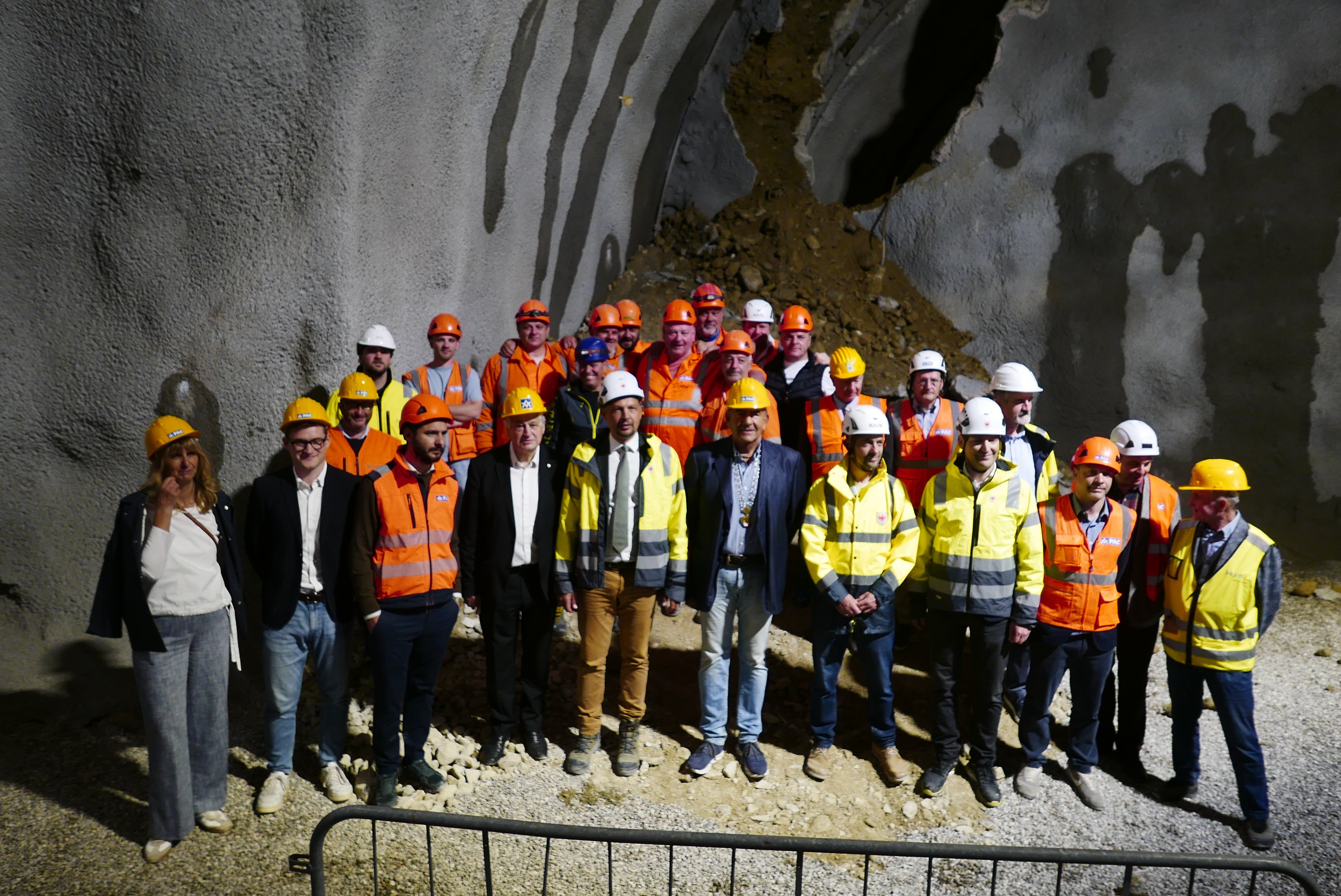 La foto simbolica appena avvenuto l'abbattimento dell'ultimo diaframma del tunnel. L'assessore provinciale Alfreider (quinto da sinistra in prima fila) ha sottolineato: “Con questo abbattimento facciamo un passo concreto verso un obiettivo molto chiaro: alleggerire il centro di Chienes, aumentare la sicurezza lungo l’asse della Pusteria e migliorare la qualità della vita delle persone che vivono qui”. (Foto: USP/Ingo Dejaco)