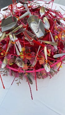 Fiori legati intervallati da forchette, coltelli, cucchiai e altri utensili da cucina. (Foto: USP/Scuola professionale per l'economia domestica e agroalimentare Aslago)