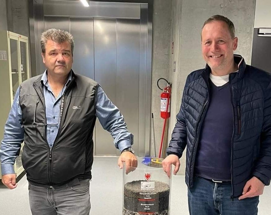 L'assessore Massimo Bessone con il geologo Volkmar Mair, vicedirettore della Ripartizione Edilizia e servizio tecnico, con un cilindro contenente i materiali di costruzione di una strada (Foto: ASP)