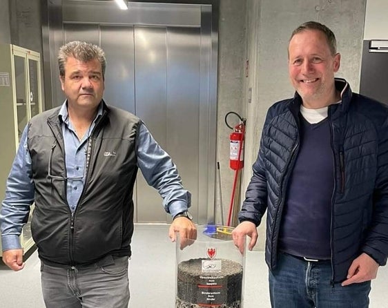 L'assessore Massimo Bessone con il geologo Volkmar Mair, vicedirettore della Ripartizione Edilizia e servizio tecnico, con un cilindro contenente i materiali di costruzione di una strada (Foto: ASP)