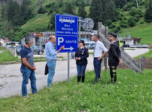 Der Direktor des Straßendiensts Götz Rufinatscha, Bürgermeister Giorgio Costabiei, die Leiterin der Straßenpolizei in Südtirol Katia Grenga, Landesrat Daniel Alfreider und Carabinierimajor Innocenzo Colonna besprechen die neue Beschilderung in Pikolein, die Besucher informieren soll, dass das Auto kostenfrei geparkt und der Bus genutzt werden kann, um aufs Würzjoch zu gelangen. (Foto: LPA/Angelika Schrott)