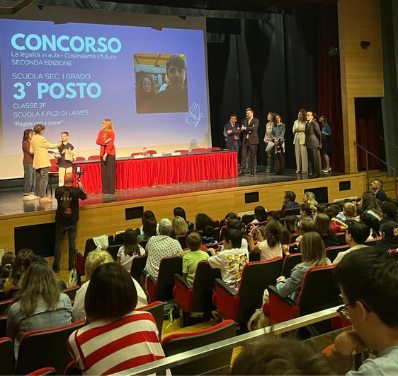 Un momento di una delle premiazioni dell'evento dedicato alla promozione della cultura della legalità tenutosi il 20 maggio al Teatro Rainerum di Bolzano, al quale ha partecipato anche il vicepresidente della Provincia Marco Galateo (nella foto sul palco in piedi in attesa di consegnare un premio a ragazze e ragazzi delle scuole). (Foto: USP)