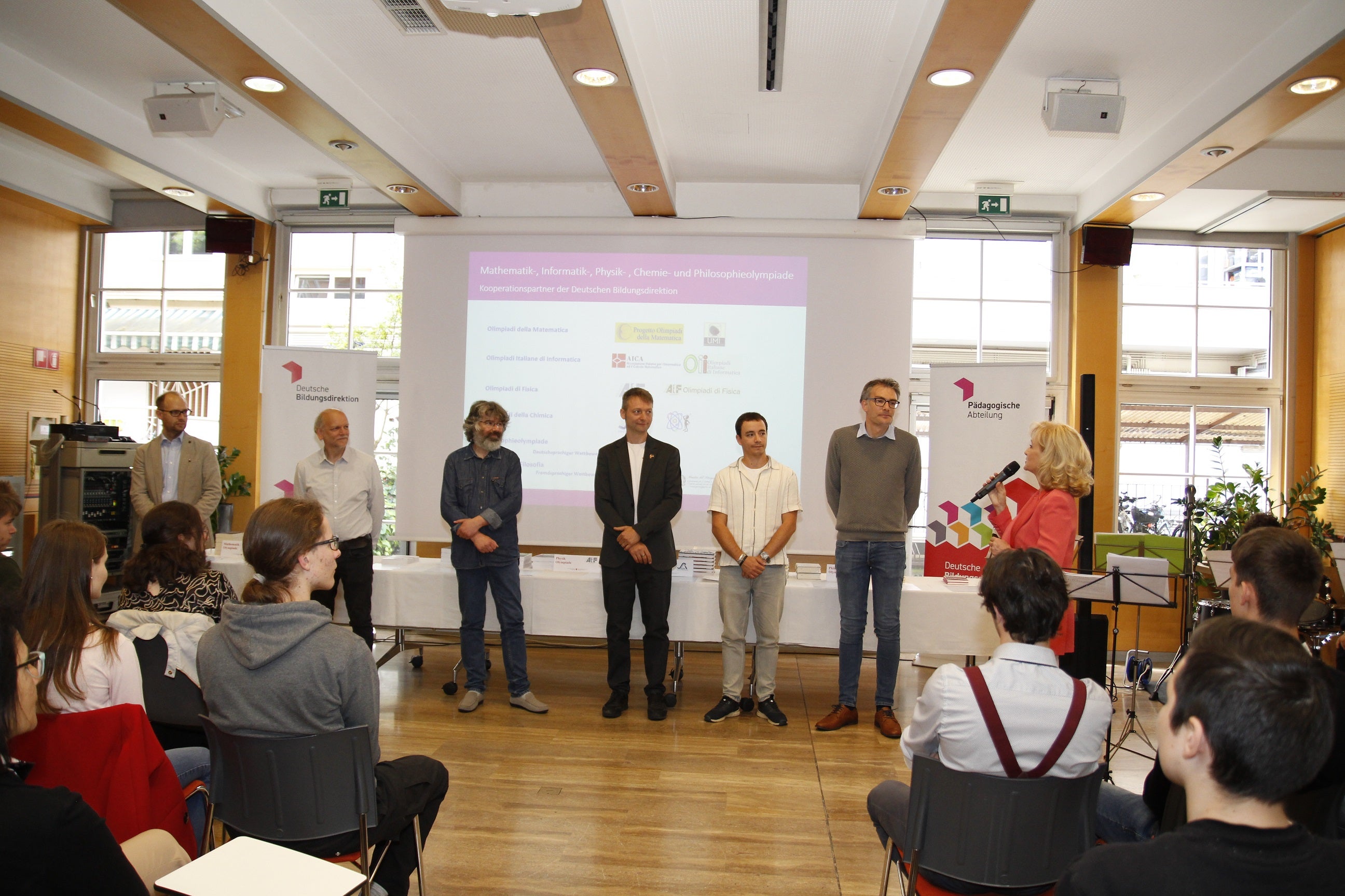 Begleitet wurden die Olympionikinnen und Olympioniken von ihren Koordinatoren (v.l.) Daniel Soraruf, Klaus Überbacher, Karl Lunger, Stefan Pilser, Alexander Ulbricht, Stefan Goller; rechts mit Mikrophon Siglinde Doblander, Koordinatorin der Begabungs- und Begabtenförderung der Pädagogischen Abteilung an der Deutschen Bildungsdirektion (Foto: LPA/Bildungsdirektion/Verena Hilber)