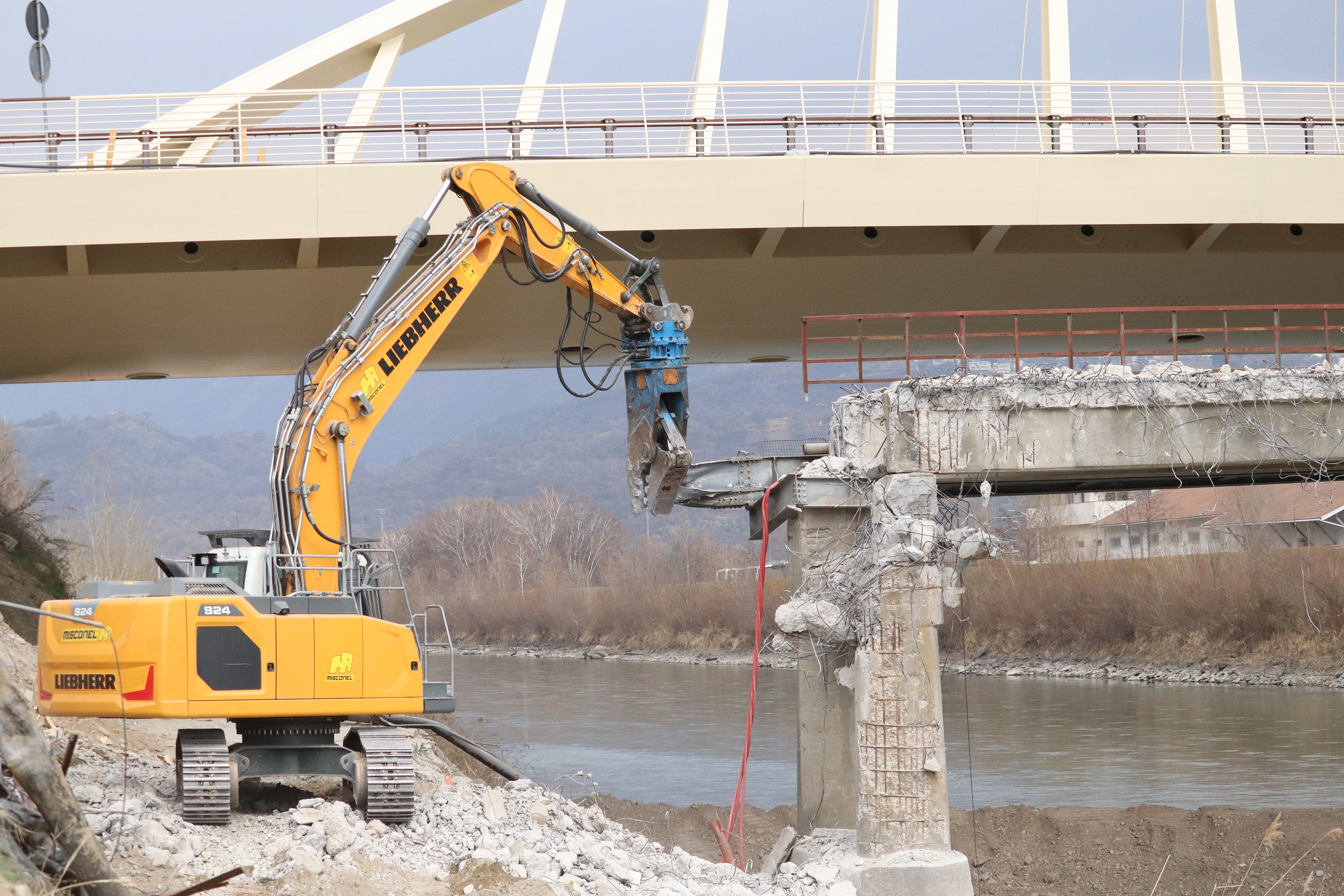 Heute hat das Bauunternehmen Misconel aus Cavalese (mit einer Niederlassung in Bozen) mit dem Abtragen der alten Brücke über die Etsch in Neumarkt begonnen; im Hintergrund die höher gelegene neue Brücke ohne Pfeiler im Flussbett. (Foto: LPA/Maja Clara)