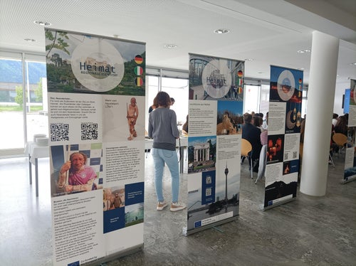 Einblick in die Wanderausstellung Heimat – regionale Identität in Europa mit Publikum im Hintergrund bei der Ausstellungseröffnung am 5. Mai im Oberschulzentrum Mals (Foto: LPA/Fachschule Tisens)