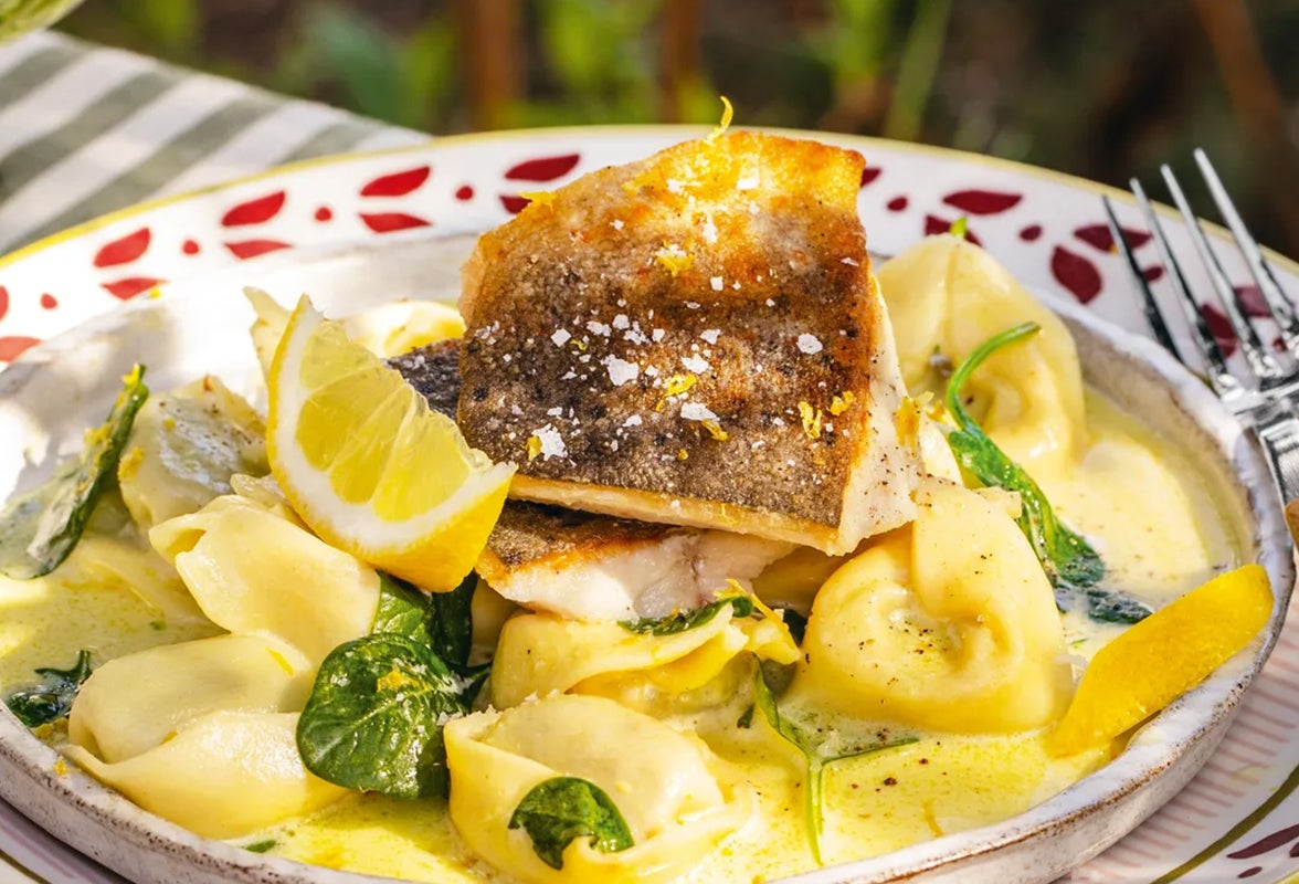 Gebratene Bachforellenfilets mit Spinat-Ricotta-Tortelloni in Zitronensauce auf Teller angerichtet