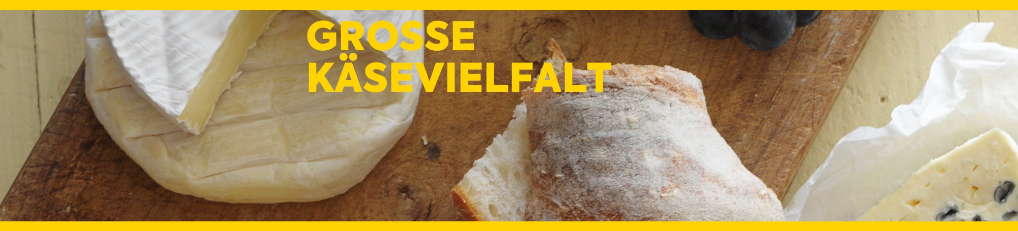 Holzbrett mit Weichkäse, Weißbrot und roten Trauben. Text: Große Käsevielfalt