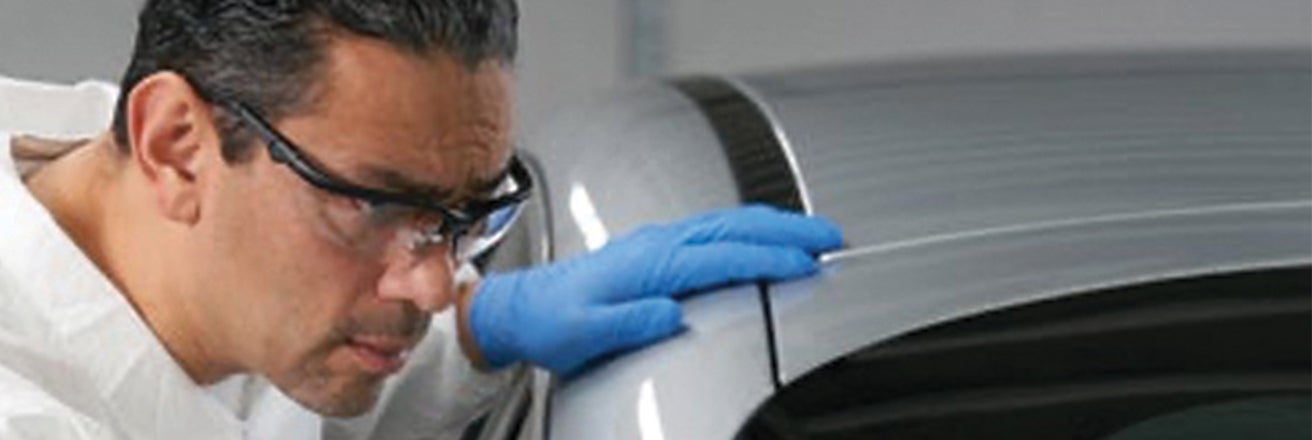 Worker wearing PPE inspecting car bodywork