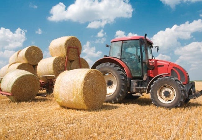 Tractor coated with red paint alongside bales of hay