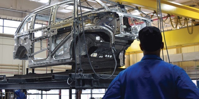 Engineer in blue uniform observing the assembly of a car chassis in an industrial manufacturing plant