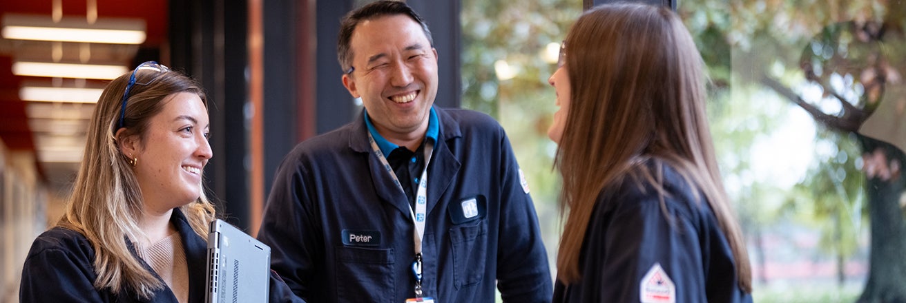 Three PPG employees chatting and smiling alongside large window overlooking trees