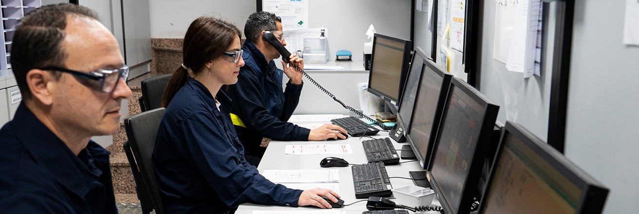 Three colleagues working on computers wearing PPE