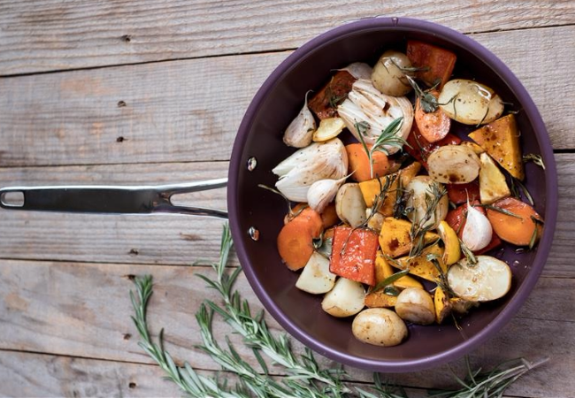 Fusion Pro coated pan with cooked mixed vegetables sitting on a wooden table surface with green herbs