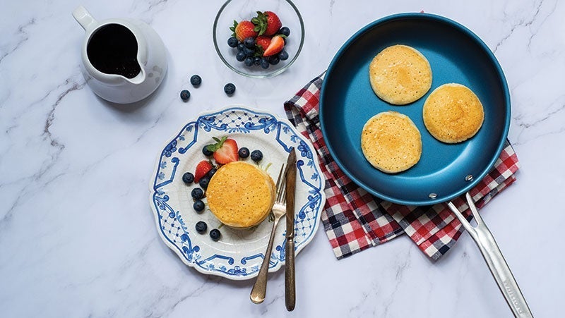 Elegant breakfast spread on marble surface featuring fluffy pancakes with berries, a blue ceramic plate, and a cup of black coffee
