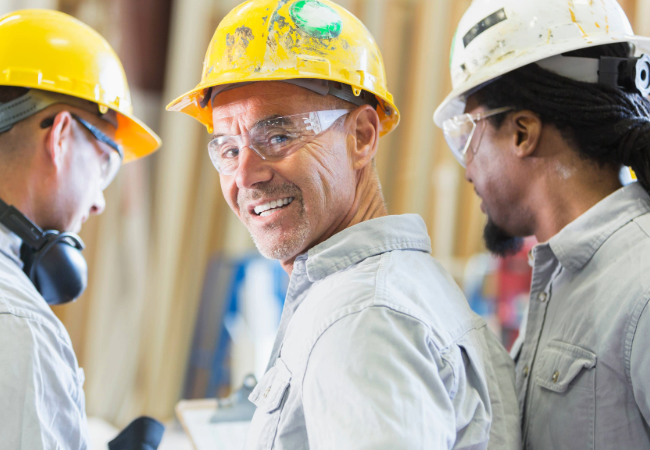 Three men in grey uniforms and hard hats studying program outlines on clipboards