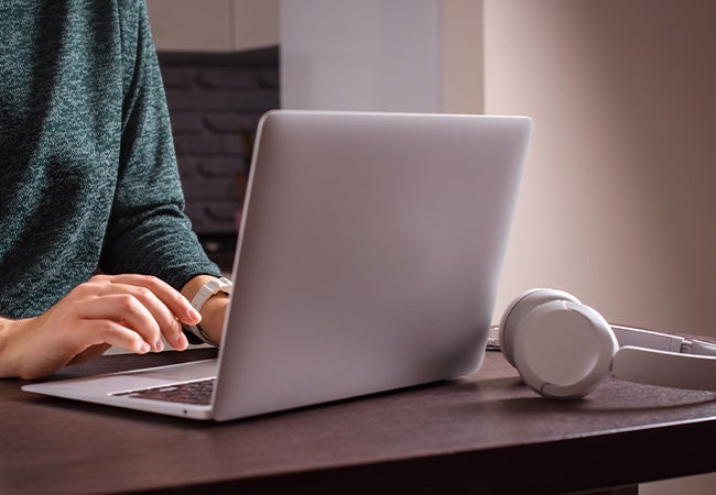 Woman sat at a table wearing a green jumper typing on a laptop with headphones coated using grey excimer technologies