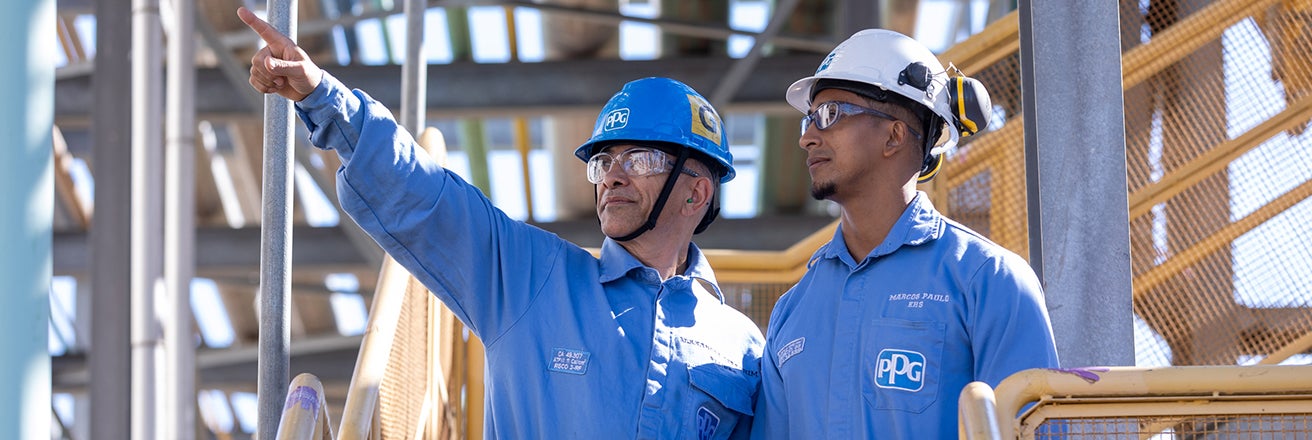 Two male workers wearing safety equipment examining a steel structure