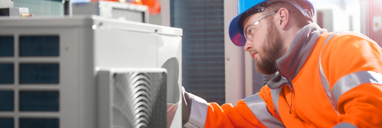 Man wearing a blue hard hat and orange workwear looking at an industrial ventilation system